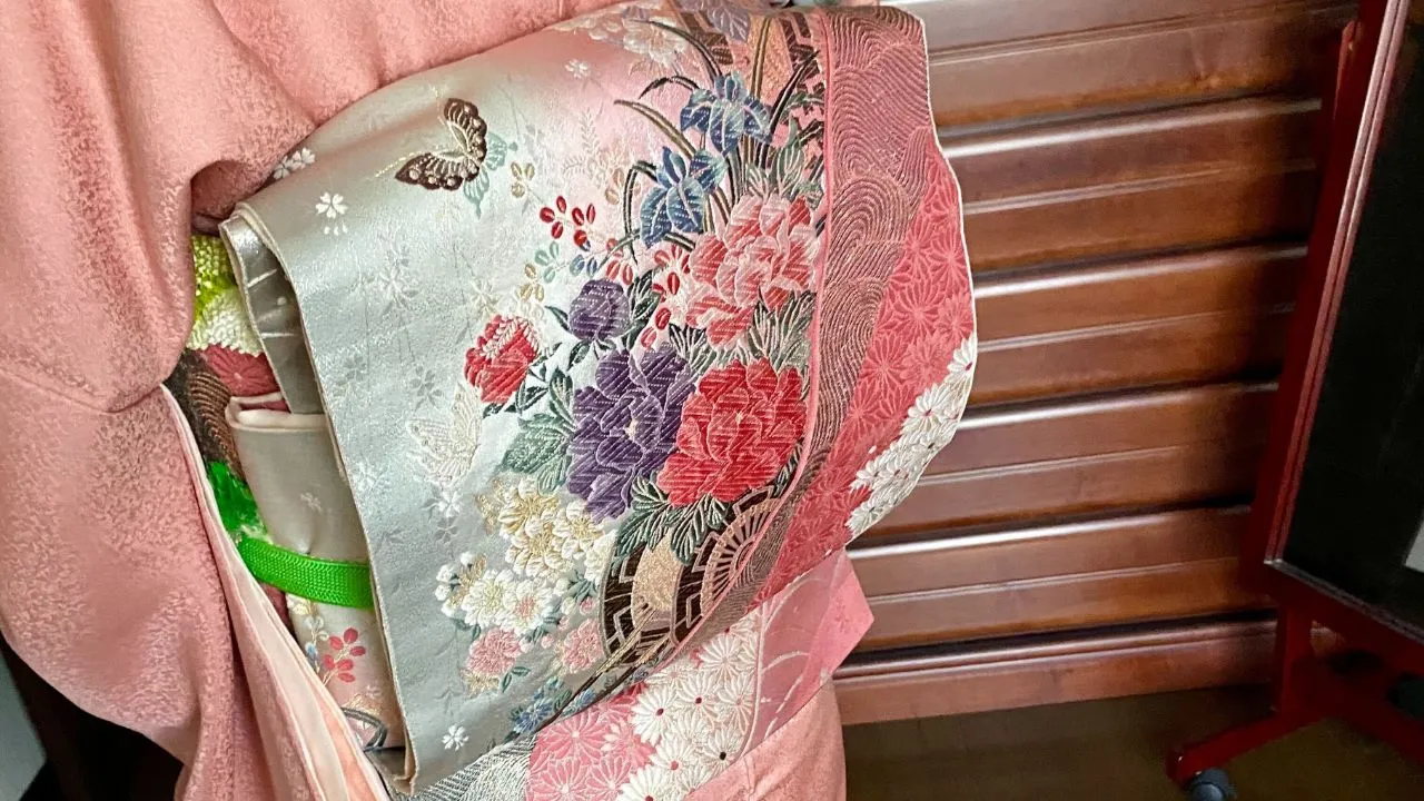 A close-up of a pink furisode kimono with an embroidered obi featuring irises, peonies, and a butterfly motif
