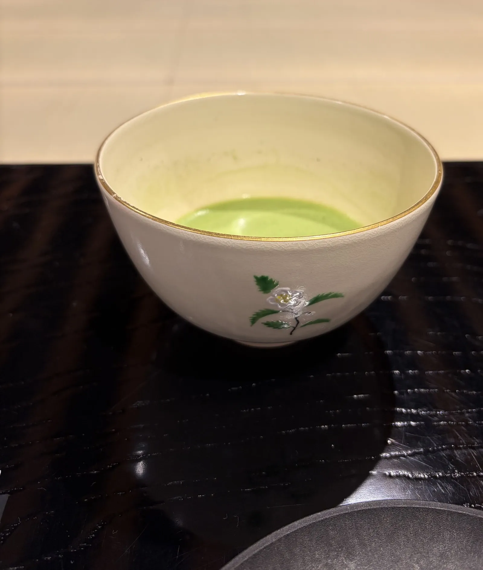 A white chawan with a painted floral motif holding freshly whisked usucha, on a dark lacquer table