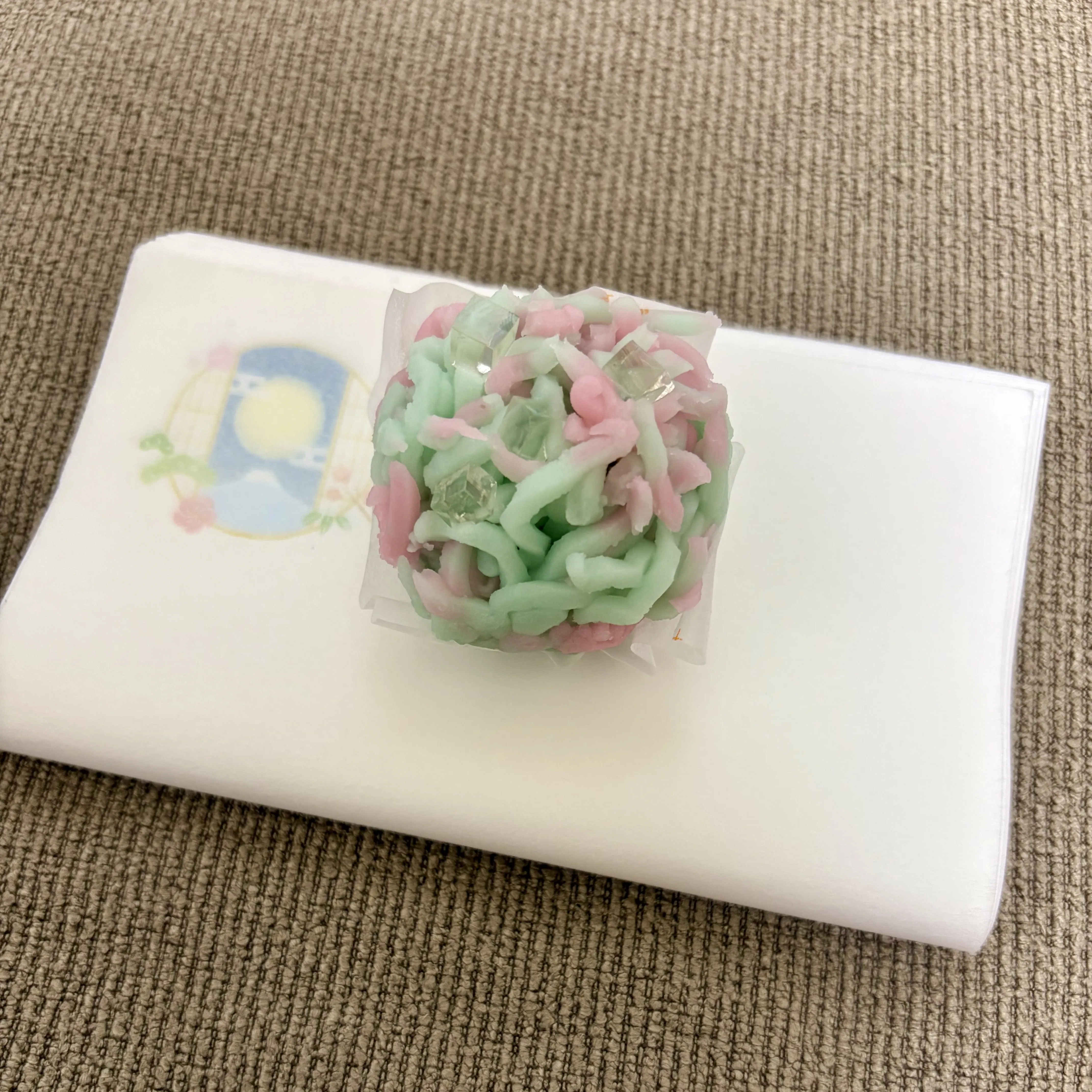 A pink and green nerikiri wagashi shaped like a chrysanthemum on a black lacquer tray
