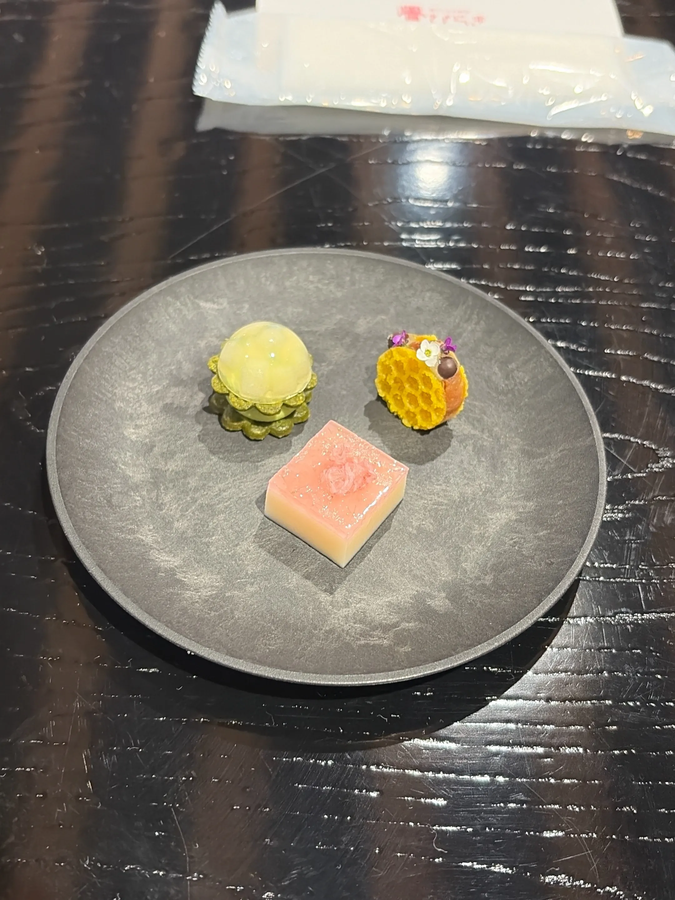 A trio of soft nerikiri wagashi sweets in seasonal shapes and colors, arranged on a black lacquer tray