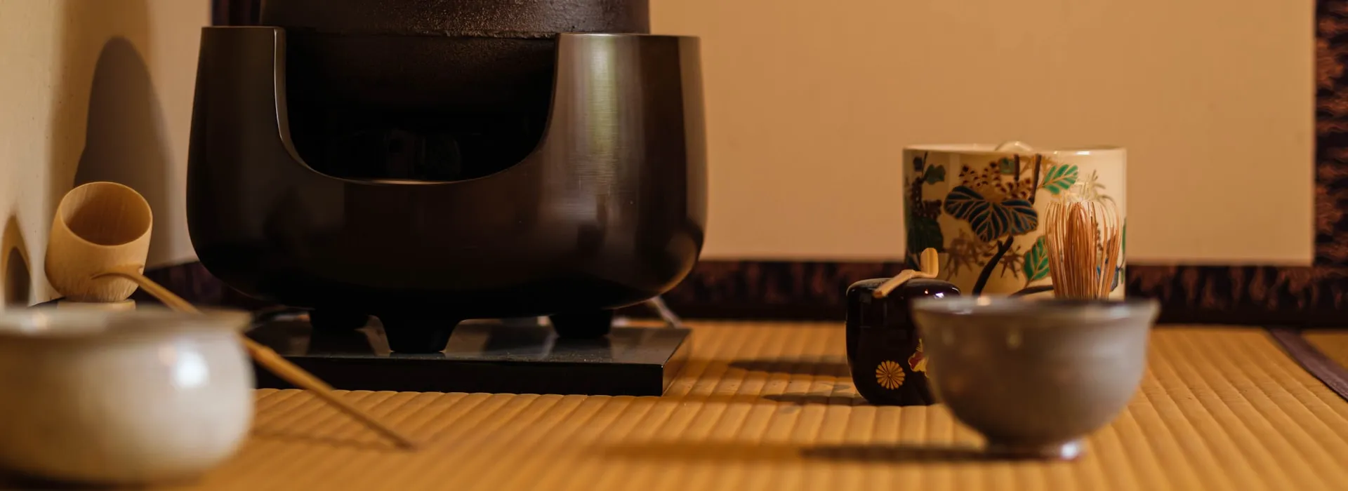 A traditional tea ceremony setup on tatami mats, with an iron kettle, bamboo whisk, and chawan bowls